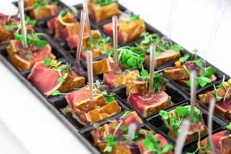 Grilled tuna chunks served with fresh green herbs on black starter plate.の写真素材