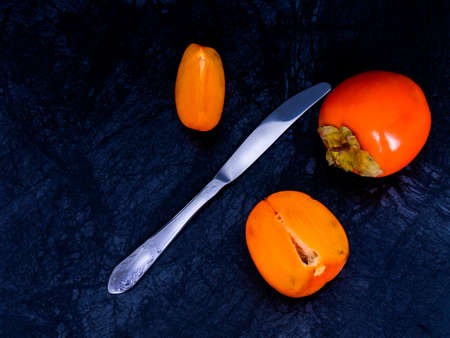 Ripe persimmons on a dark background, divided with a knife.の写真素材