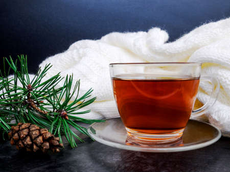 Glass cup of hot tea, dressed in knitted warm scarf winter warm knitted sweater or blanket. Still scarf and a cup of tea with Christmas tree. In the winter time. Cozy and soft winter background.の写真素材