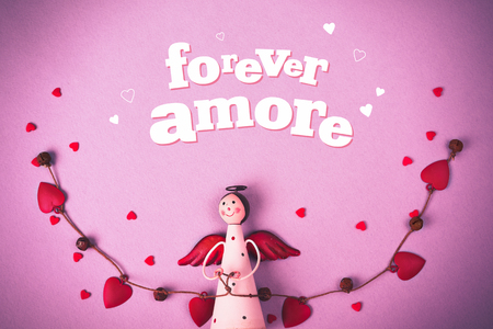 Levitating Angel with hearts and bells. Symbol of love. The concept of Valentine's Day. Inscription Forever Amore. Pink backgroundの写真素材