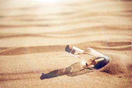A bottle with a message is thrown by a wave on a sandy beach. Sandy background. A sunny hot day Copy spaceの写真素材