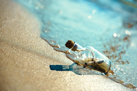A bottle with a message is thrown by a wave on a sandy beach. Sandy background. The bottle floats in the surf line.の写真素材