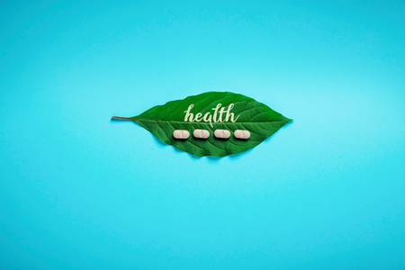 Green leaf with the inscription of health and herbal pills, on a blue background. Concept of health, minimalism.の写真素材