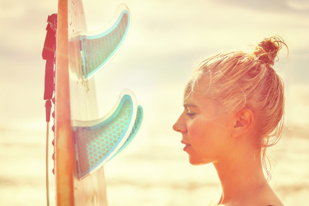 Beautiful girl surfer with a board at sunrise. Summer vacation at sea, healthy lifestyle.の写真素材
