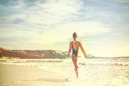 Beautiful sexy and sporty girl surfer walks with a board on the beach at sunrise. Active lifestyle and recreationの写真素材