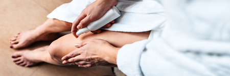 The girl in the bathroom puts anti-cellulite cream, serum on the legs and body. Body care concept. Top View. Bannerの写真素材