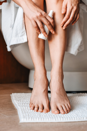 Body care. A young woman in the bathroom applies natural cream to her legs. Cosmetics and anti-cellulite careの写真素材