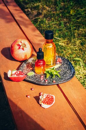 Trendy sunlight pomegranate seed oil, whey in different bottles on wooden background. Concept of anti-aging organic skin care. Ripe pomegranates lie nearbyの写真素材