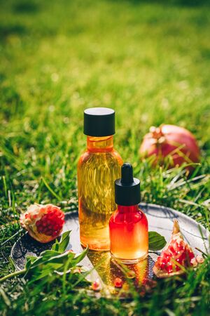 Pomegranate seed oil, serum in glass bottle on a decorative grater, on green grass background. Flat lay, minimalism. Concept of anti-aging organic skin care.の写真素材