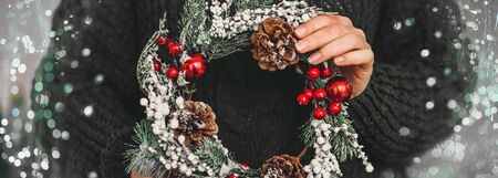 Pine wreath and Christmas decor in female hands on a green knitted background. New Year preparation Bannerの写真素材