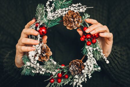 Pine wreath and Christmas decor in female hands on a green knitted background. Christmas, New Year preparationの写真素材