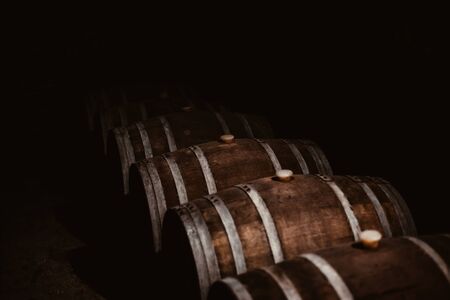 Vintage old oak barrels of wine, cognac in the wine dark vaults of the winery. Selective soft focus....