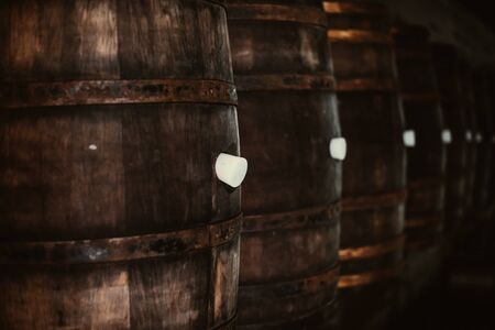 Vintage old oak barrels of wine, cognac in the wine dark vaults of the winery. Selective soft focus. Shooting in the darkの写真素材