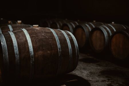 Vintage old oak barrels of wine, cognac in the wine dark vaults of the winery. Selective soft focus. Shooting in the darkの写真素材