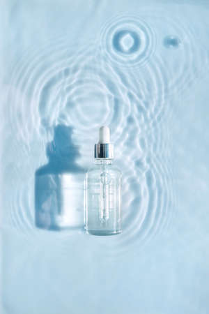 Cosmetic spa medical skin care, bottle for serum, micellar toner and emulsion on water texture background with splashes. Flat lay, copy space.の写真素材