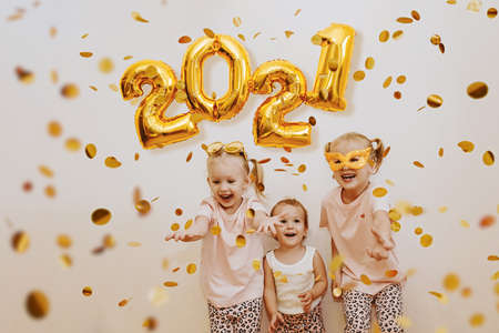 Three little girls are enjoying the flying golden confetti. Celebrating at home 2021. Concept for...