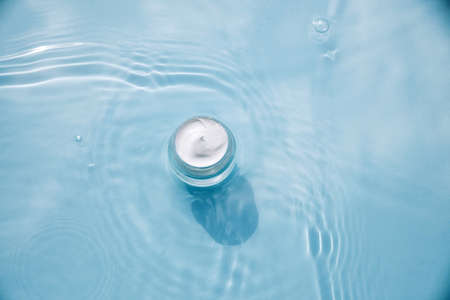 Cosmetic product on water with splashes. Jar with cream on aqua background, advertising natural...