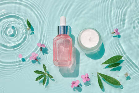 Set moisturizing cosmetic products on water with drops. Serum glass bottle and cream on aqua surface