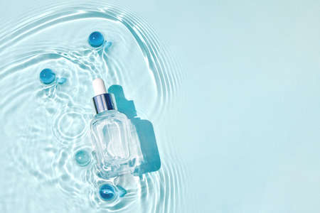 Mockup of cosmetic glass blue bottle with pipette and serum on water surface with wavesの写真素材