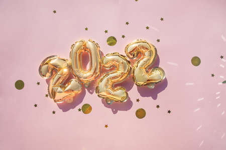 Gold balloons 2022 on pink background, confetti New Years concept