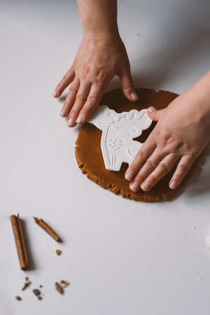 Female hands with a deer shape cutter cut out gingerbread cookies from doughの写真素材