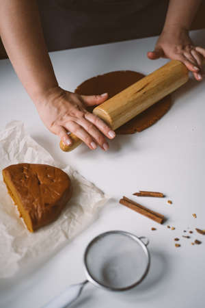 Female hands roll out raw ginger dough with a rolling pin on a white tablの写真素材