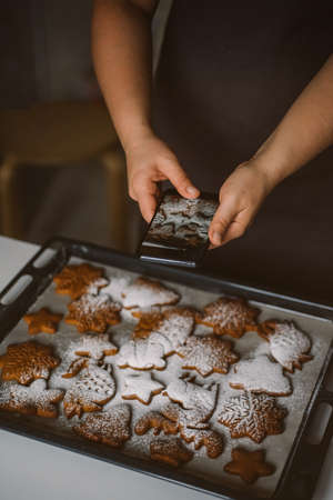 Woman takes photo on smartphone Christmas gingerbread sprinkled with powdered sugar.の写真素材