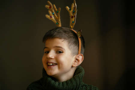 Cute boy in green sweater and antlers makes a faceの写真素材