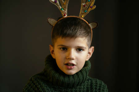 A cute boy in a green sweater and antlers makes a faceの写真素材
