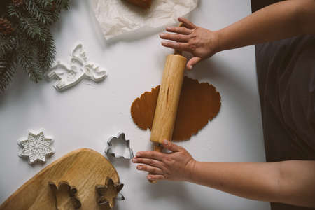 Female hands roll out raw ginger dough with a rolling pin on a white tabl