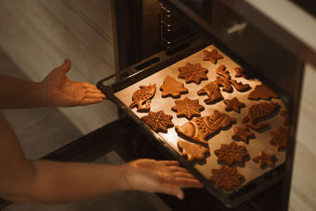 Baker places a baking sheet with gingerbread cookies in the ovenの写真素材