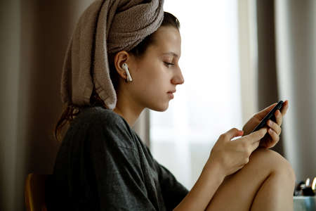 Teenage girl in turban made of towels in living room looks in smartphoneの写真素材