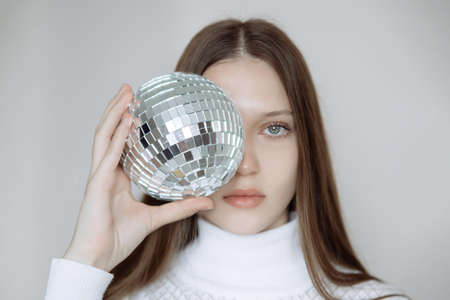 Fashion portrait of a teenage girl with a disco ball, covering her faceの写真素材