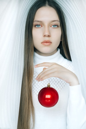 Girl with expressive eyes in a snow-white dome with a bright red Christmas ballの写真素材