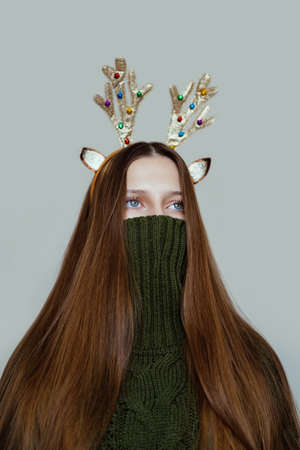 Surreal Christmas portrait of a girl in a green sweater and antlersの写真素材