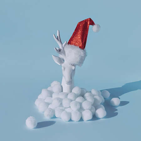 Figurine of a deer head in a Santa Claus hat in artificial snow on blue backgroundの写真素材