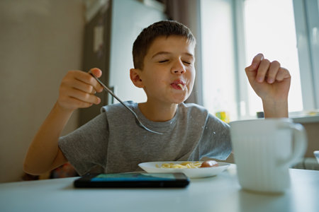 Cheerful, hungry boy eats pasta with appetite, sucks in pasta playfullyの写真素材
