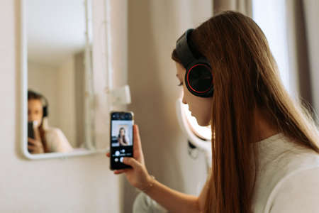 Teenage girl in headphones in front of the mirror takes selfie, admires.の写真素材