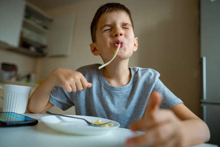 Boy, child eating macaroni, retraction long pasta into his mouthの写真素材
