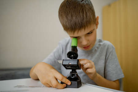 Boy 7 years old, at home in the room looks through microscopeの写真素材