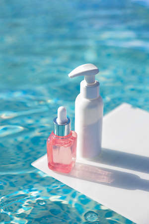 Bottle with serum, white package on background of blue water of pool Cosmetics with for moisturizingの写真素材