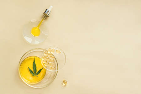 CBD oil in a pipette, THC tincture in laboratory round cups and marijuana leaves on light backgroundの写真素材