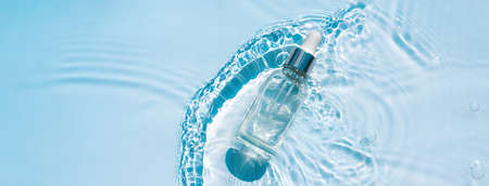 Moisturizing serum with hyaluronic acid in a transparent bottle with a pipette on a transparent water blue background with waves and ripplesの写真素材