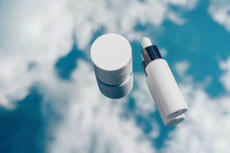 Natural oxygen cosmetics, white mockup of a bottle with a pipette and a jar of cream on blue sky backgroundの写真素材