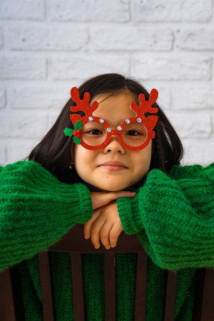Portrait of an Asian girl in a green sweater and masquerade red glasses with deer hornsの写真素材