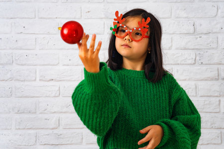 Asian girl in masquerade glasses with reindeer horns, playing with a Christmas ballの写真素材