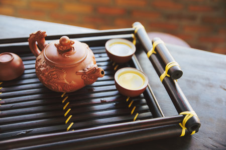 Brown ceramic pot and brown cup .Green tea on bamboo mat, aged wooden tableの写真素材