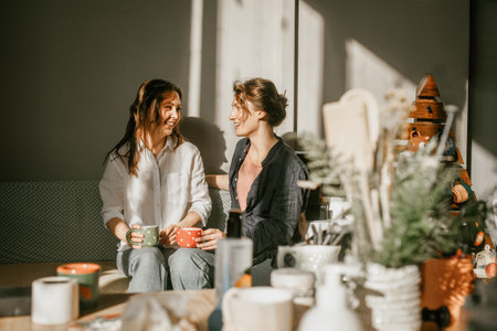 Time for intimate conversations: two women drinking tea in the sunshine in a cozy environment Girls friends talking over a cup of coffeeの写真素材