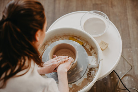 Forming the walls of a clay product on a potters wheel. Pottery, female hands of a potter create a product from white clay. Top viewの写真素材