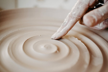 Decorating wet clay on a potters wheel with a wine groove. A potter draws a spiral with his finger on the bottom of a white clay plate. Abstract clay background Macroの写真素材
